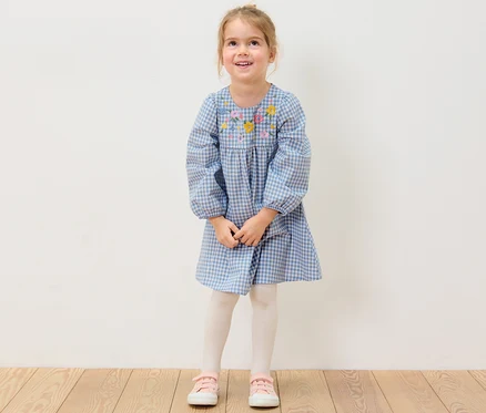 Ein lächelndes Mädchen trägt ein gewebtes Kinderkleid mit Blumenstickerei.