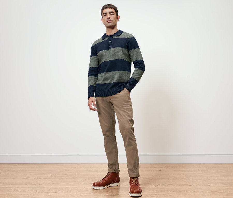 Mann posiert in Pullover und sandfarbener Chino.