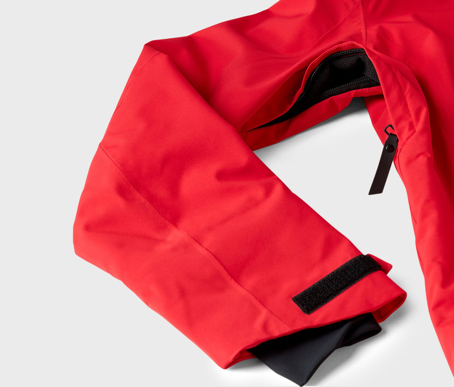 Detail einer roten Jacke mit Reißverschlusstasche und Klettverschluss am Ärmel.