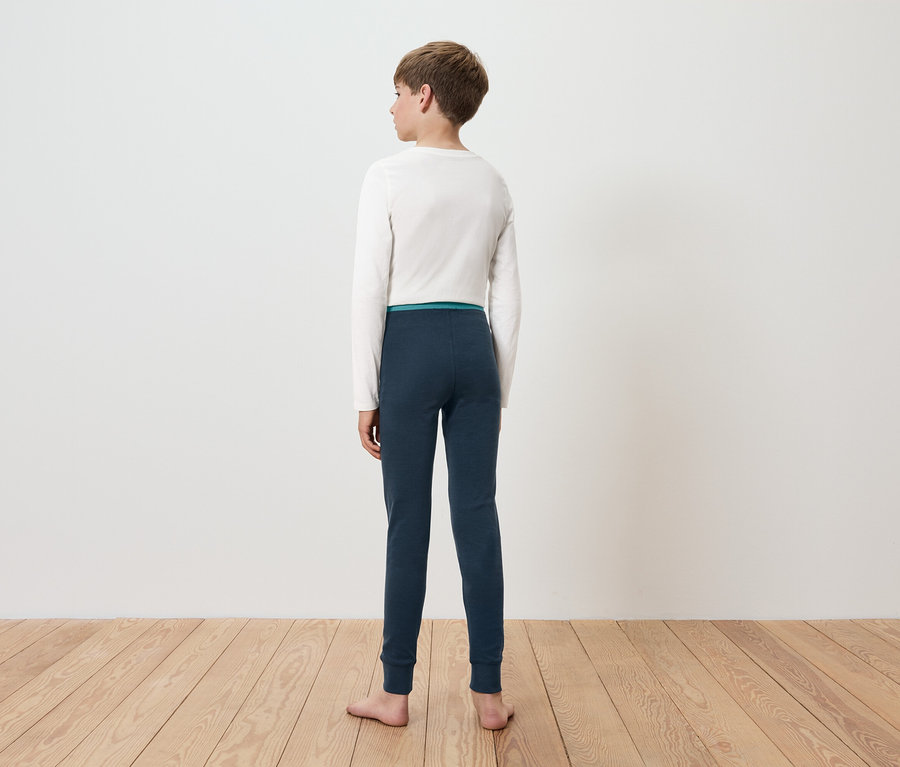 Ein Junge steht mit dem Rücken zur Kamera und trägt ein weißes Langarmshirt und blaue Leggings.