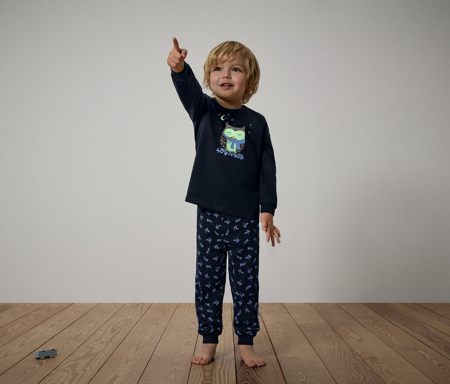 Junge im dunkelblauen Pyjama mit Eulenmuster zeigt mit dem Finger nach oben.
