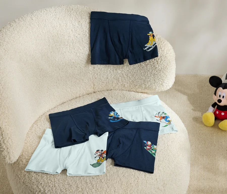 Auf einem beigen Sessel liegen fünf Boxershorts mit Aufdruck. Neben dem Sessel sitzt ein Mickey Mouse Plüschtier mit einem Fußball.