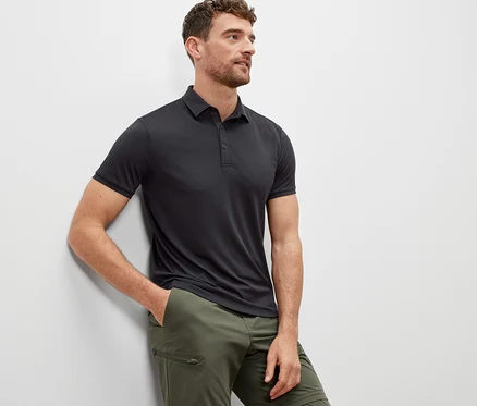 Mann lehnt an einer Wand und trägt ein anthrazitfarbenes Funktions-Poloshirt.