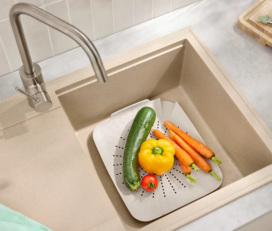 Im Spülbecken befindet sich ein flaches Spülbecken-Sieb mit Karotten, Paprika, Zucchini und Tomate.