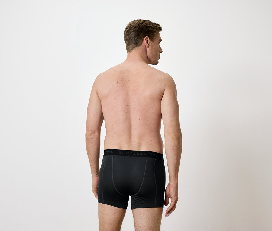 Rückansicht eines Mannes in schwarzen Boxershorts vor einem weißen Hintergrund.