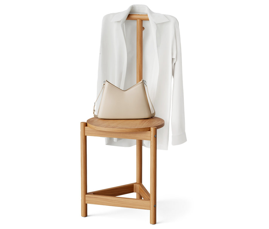 Eine beige Handtasche und ein weißes Hemd liegen auf einem Holzhocker.