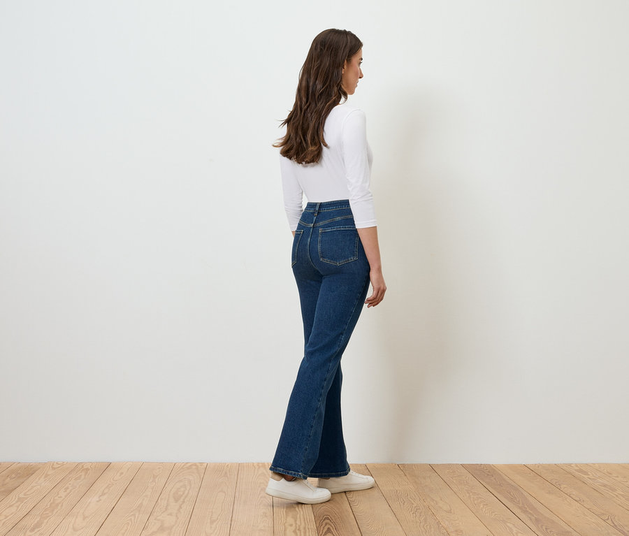 Frau posiert in Jeans und weißem Oberteil.