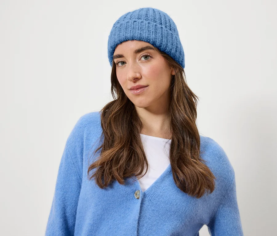 Porträt einer Frau mit braunen Haaren, die eine blaue Strickmütze und einen Cardigan trägt.