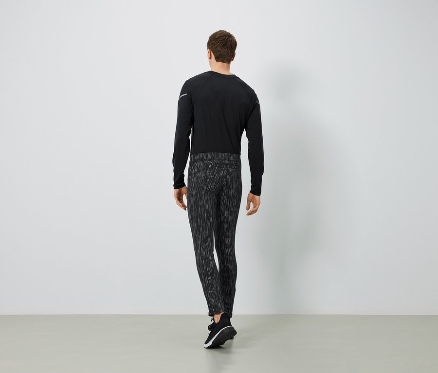 Ein Mann in einem schwarzen Langarmshirt und gemusterten Hosen, von hinten gesehen.