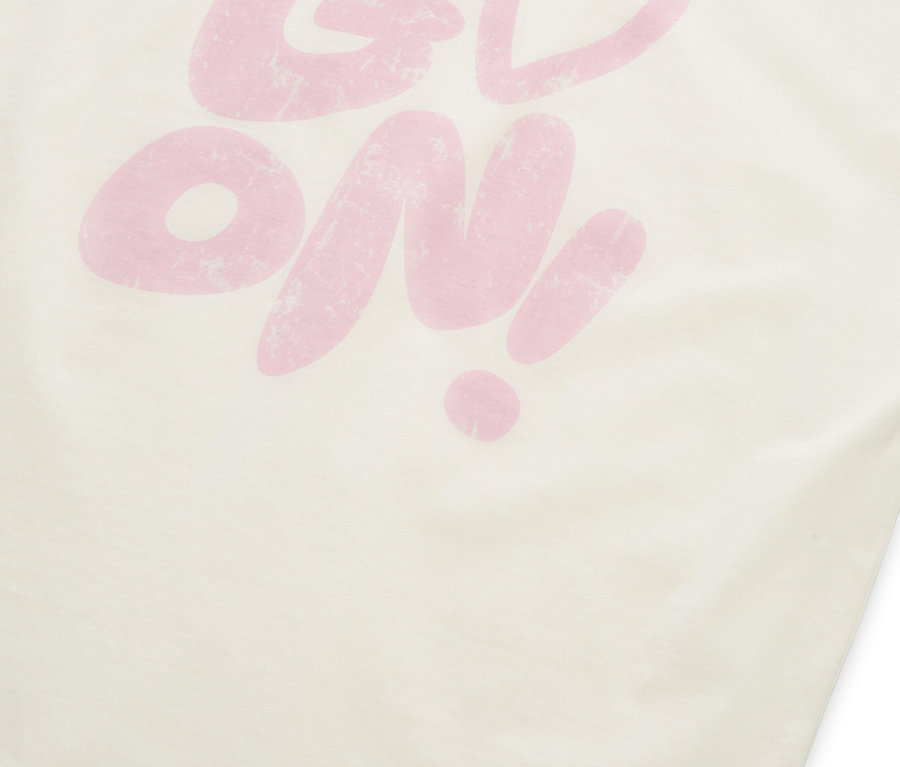Ein cremefarbenes T-Shirt mit dem rosafarbenen Aufdruck "GO ON!", wobei das "O" in "GO" durch ein Herzsymbol ersetzt wurde.