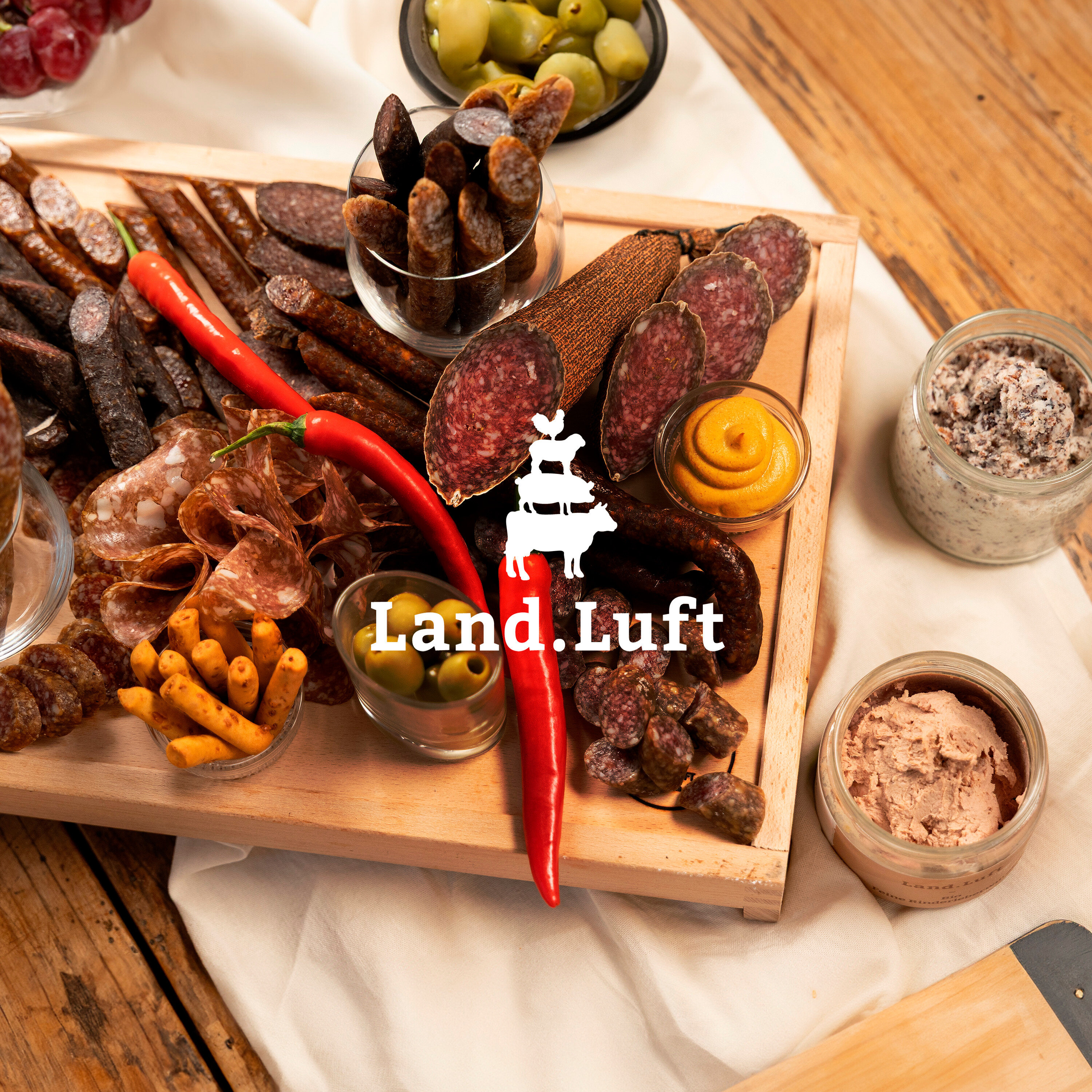 Aufschnittplatte mit Wurst, Oliven, Senf und Aufstrichen auf einem Holztisch.