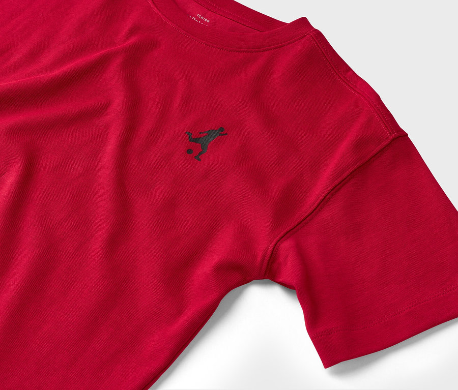 Nahaufnahme eines roten T-Shirts mit kurzem Ärmel und kleinem, dunklem Fußballspieler-Logo.