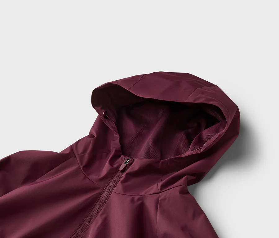 Nahaufnahme einer weinroten Jacke mit Kapuze und Reißverschluss vor einem weißen Hintergrund.