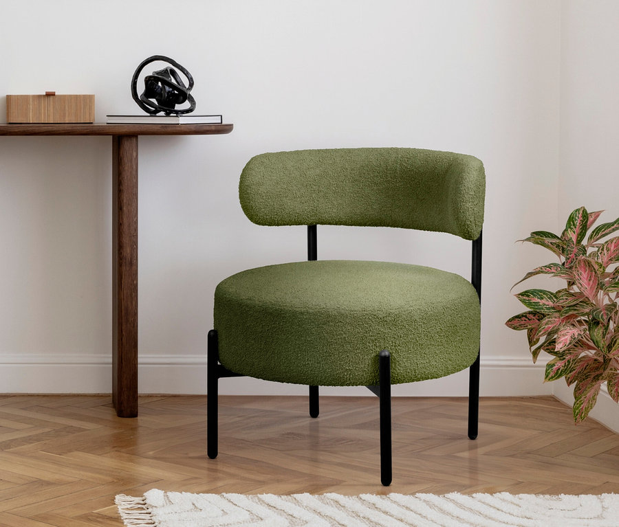 Ein grüner Sessel mit schwarzen Beinen steht auf einem Teppich neben einem Holztisch.
