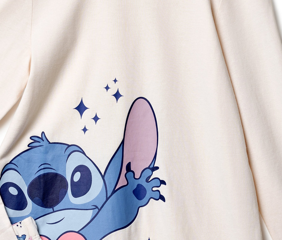 Detailansicht eines cremefarbenen Oberteils mit einem blauen Stitch-Druck und funkelnden Sternen.