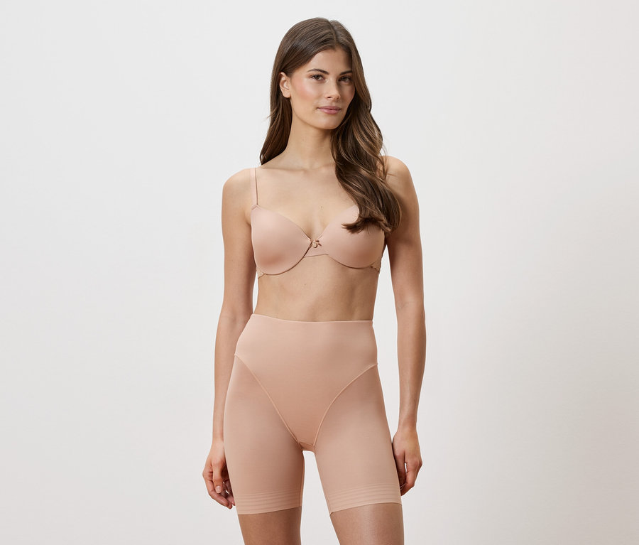 Frau trägt einen hautfarbenen BH und figurformende Shorts vor einem weißen Hintergrund.