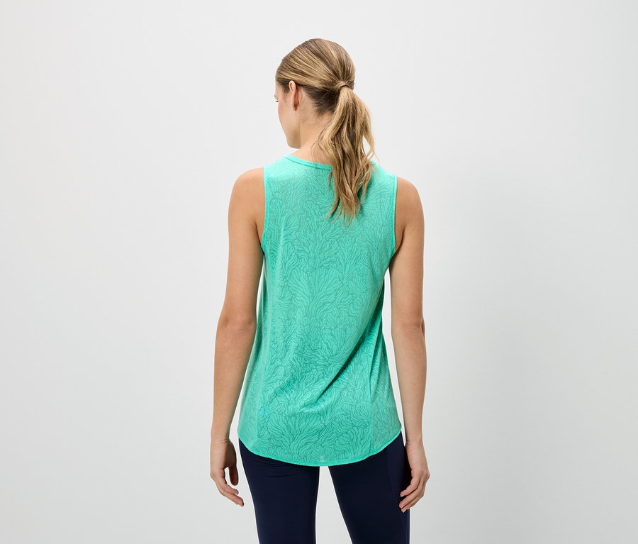 Rückansicht einer Frau mit blonden Haaren, die ein ärmelloses grünes Tanktop mit Muster und marineblaue Leggings trägt.
