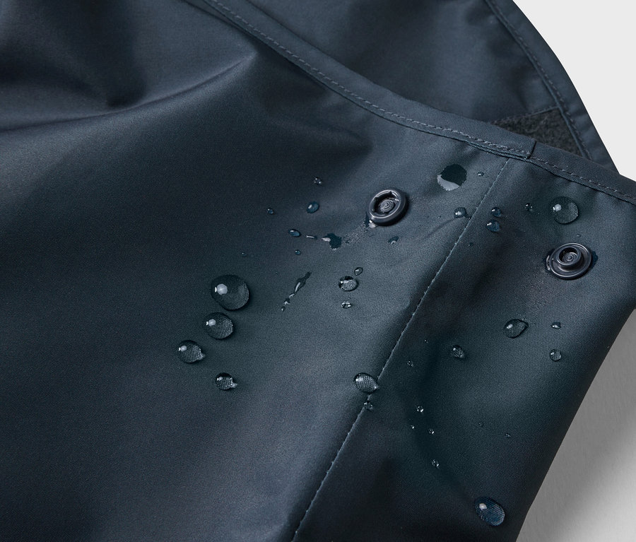 Nahaufnahme von Wassertropfen auf einem marineblauen Stoff mit zwei Druckknöpfen.