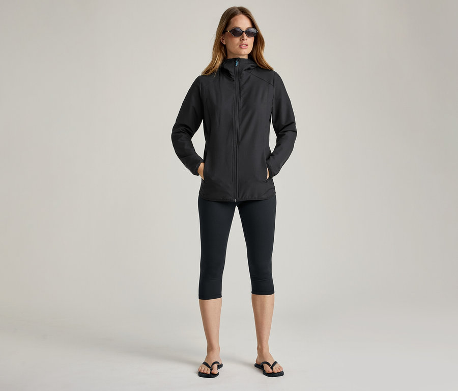 Frau mit Sonnenbrille und schwarzer Softshelljacke. Sie hat die Hände in den Taschen.