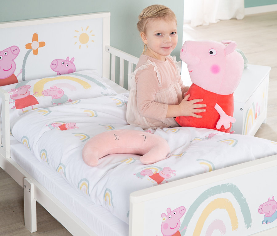 Ein kleines Mädchen sitzt in einem Peppa Pig Bett und umarmt ein Peppa Pig Stofftier.