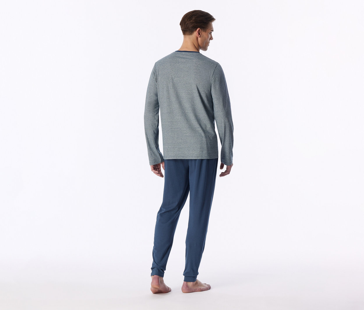Mann von hinten, trägt ein graues Langarmshirt und eine blaue Jogginghose, barfuß auf weißem Hintergrund.