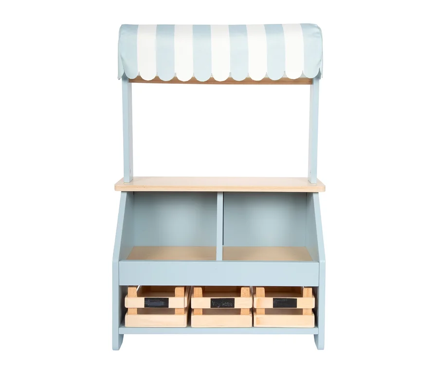 Ein small foot kompakter Kaufladen in Hellblau und Naturholz mit gestreiftem blau-weißem Vordach, Theke, zwei offenen Fächern und drei Holzkisten mit Kreidetafeln.
