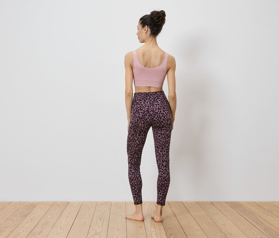 Eine Frau steht mit dem Rücken zur Kamera, sie trägt ein rosa Sportoberteil und Leggings mit Leopardenmuster.