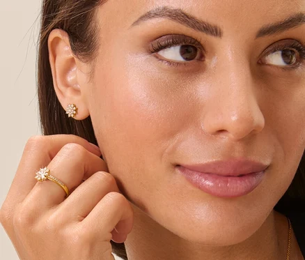 Frau berührt einen goldenen Ring mit Diamanten in Sternform. Sie trägt eine Halskette und Ohrringe im gleichen Design.
