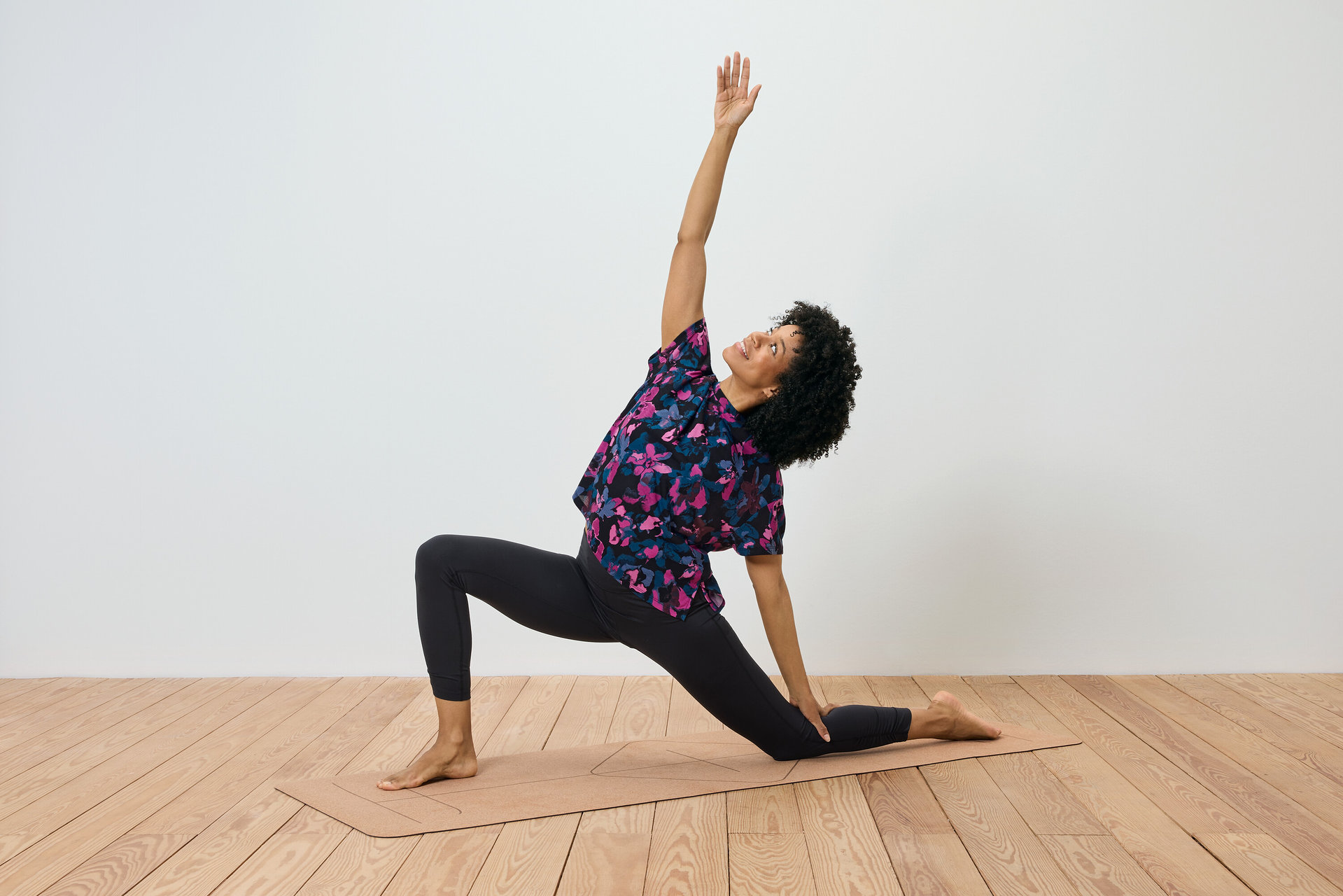 Frau mit lockigem Haar macht eine Übung auf einer Yogamatte, der rechte Arm ist erhoben und der linke berührt die Matte.