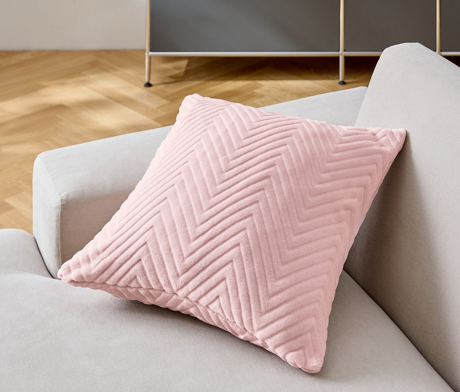 Ein rosa Zierkissen mit Chevron-Muster liegt auf einem grauen Sofa.