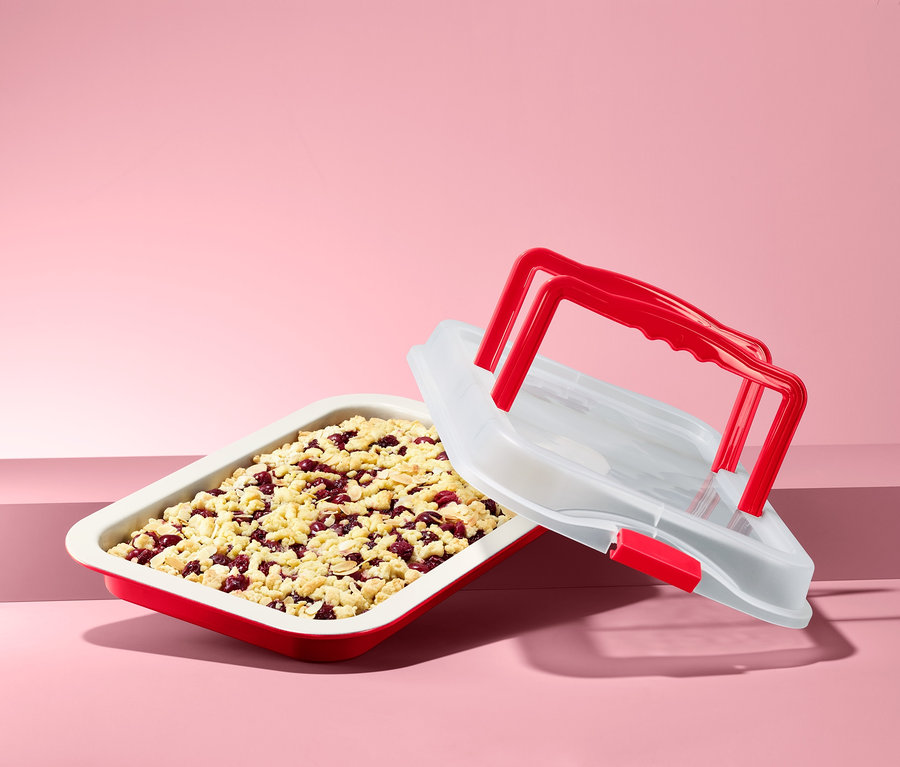 Ein rotes Backblech mit einem Obstkuchen und einem weißen Transporthaube mit rotem Griff.