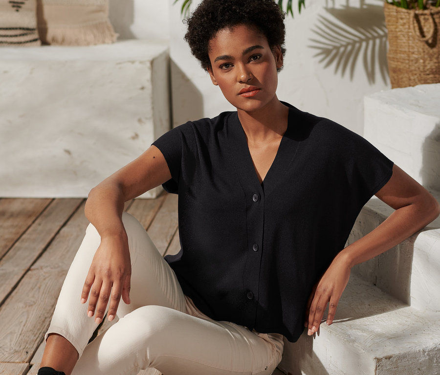 Frau sitzt auf Holzboden und trägt einen kurzärmeligen Cardigan.