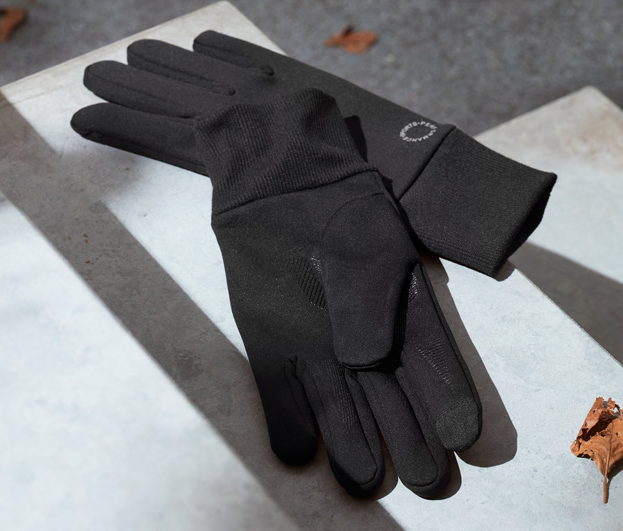 Schwarze Windprotection-Handschuhe liegen auf einer Betontreppe neben einem trockenen Blatt.