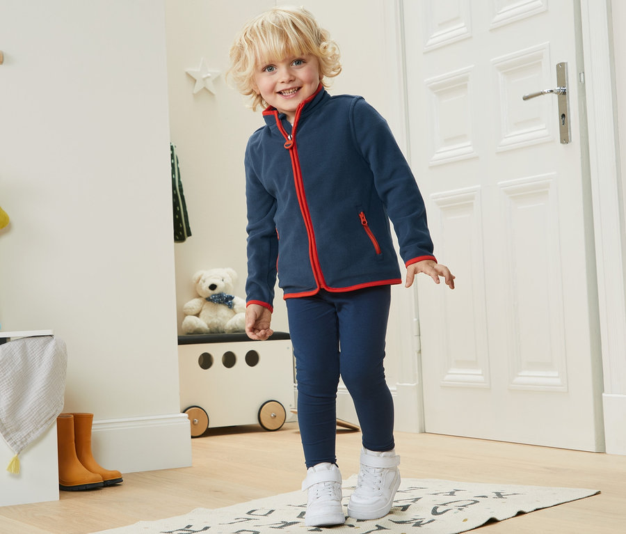 Kleiner Junge steht auf einer Matte und trägt eine blaue Fleecejacke aus recyceltem Material.