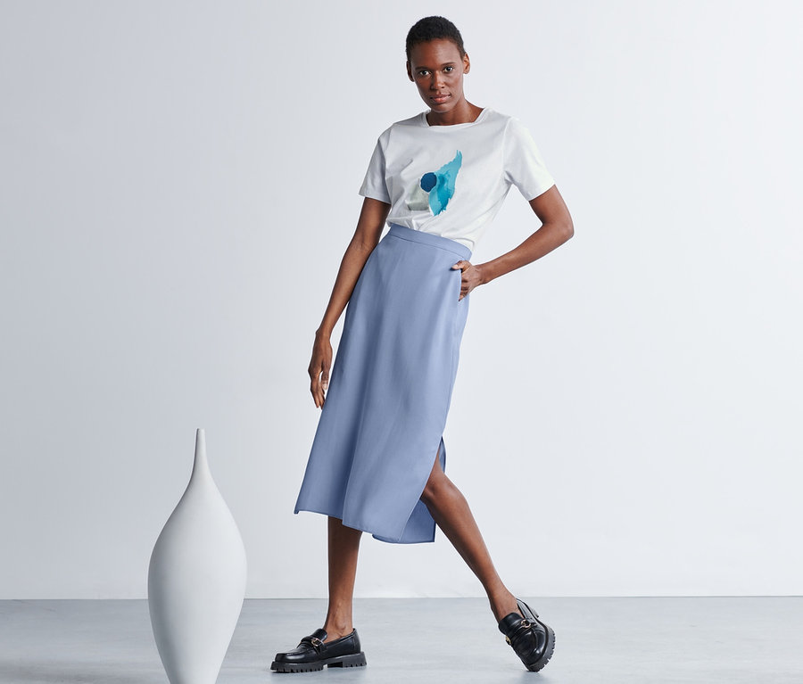 Frau posiert in weißem T-Shirt und blauem Midirock.