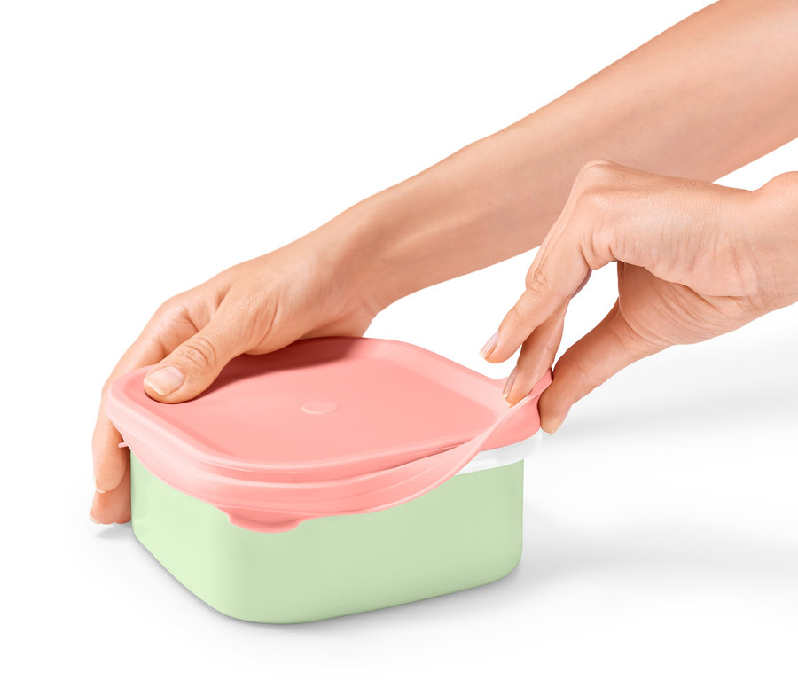 Hände öffnen eine Emaille-Lunchbox mit rosa Deckel und grünem Boden.