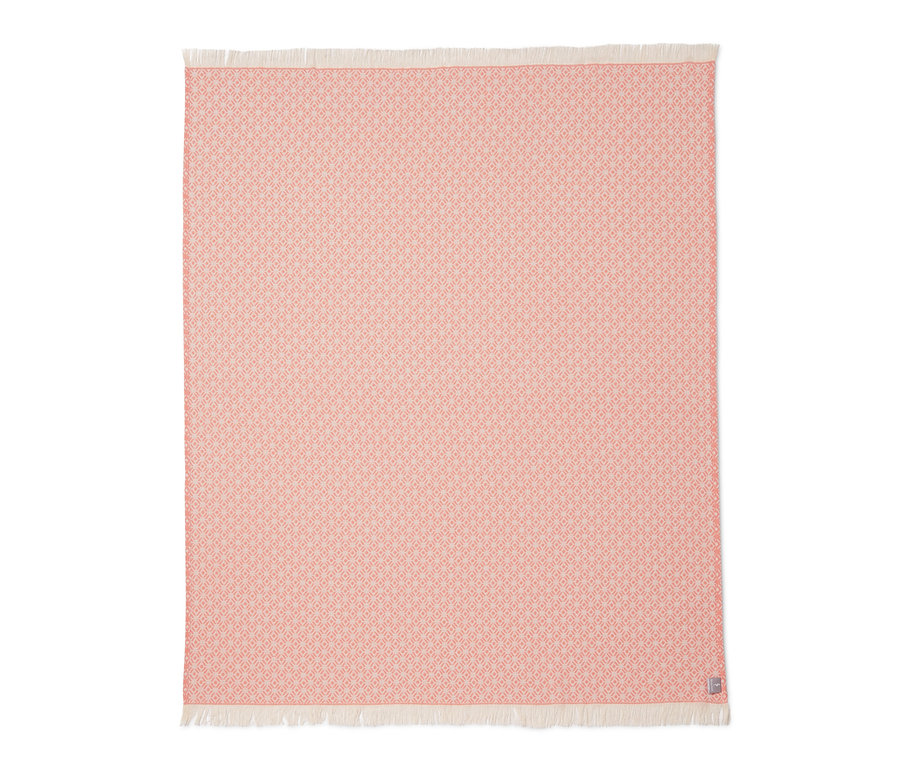 Eine rosafarbene Wohndecke mit geometrischem Muster und Fransen.