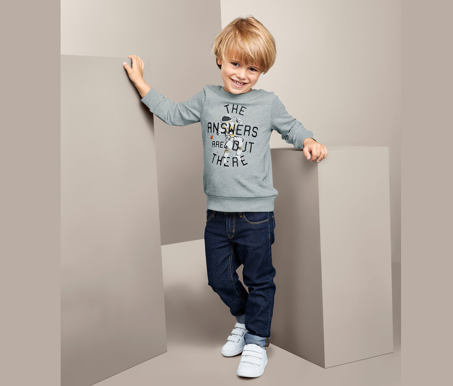 Ein Junge posiert in einem Sweatshirt mit Aufdruck, Jeans und weißen Turnschuhen.