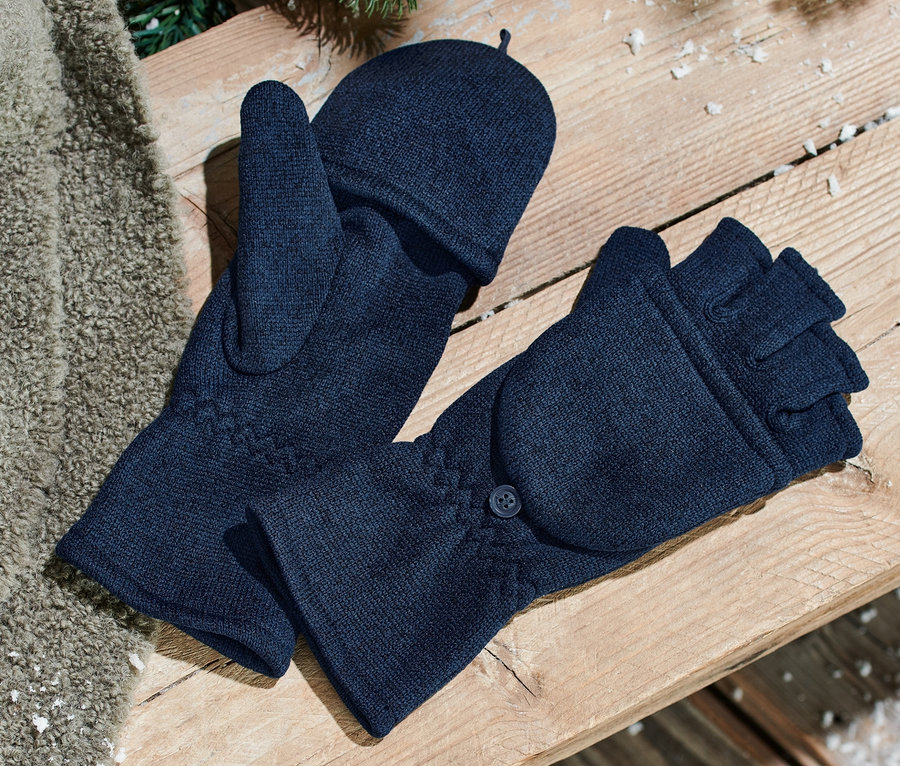 Zwei blaue Strickfleece-Klappfäustlinge liegen auf einer Holzbank. Daneben liegt eine braune Decke und Tannennadeln sind zu sehen.