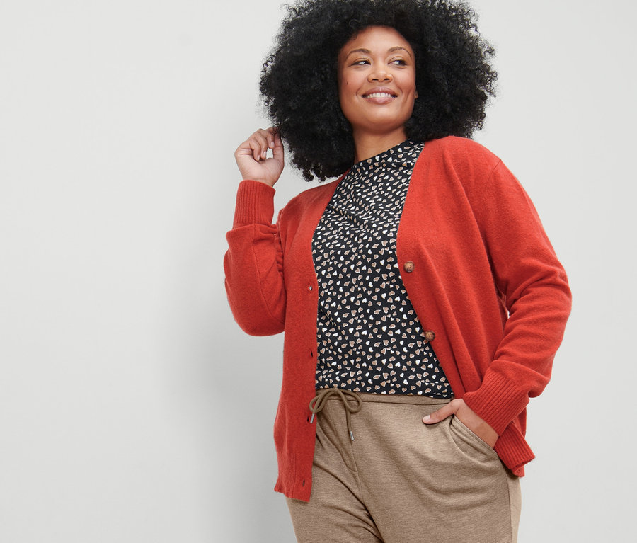 Frau posiert in Cardigan mit V-Ausschnitt, beigen Joggpants und Langarmshirt mit Alloverprint.