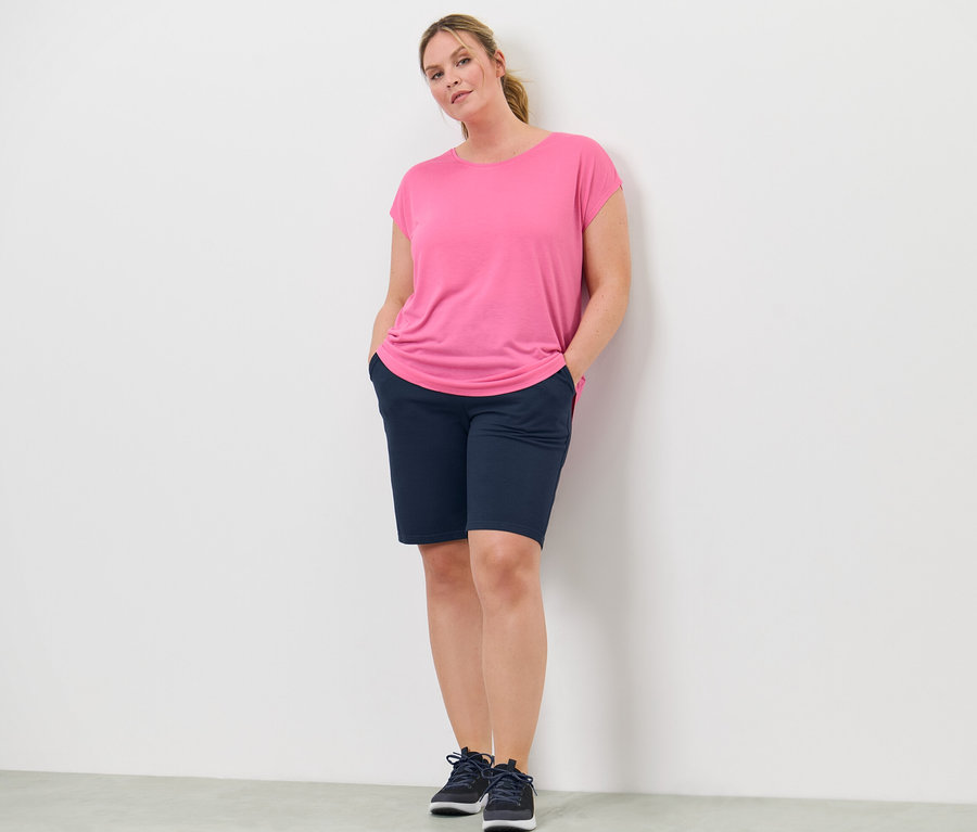 Frau steht mit Händen in den Hosentaschen. Sie trägt ein pinkes Sportshirt.