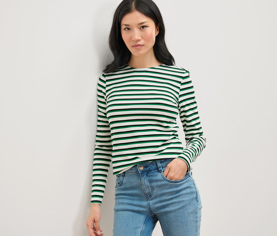 Frau posiert in einem gestreiften Langarmshirt, mehrfarbig, und Jeans.