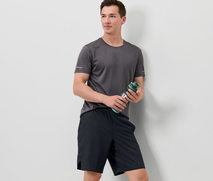 Mann hält eine Wasserflasche und trägt Sportshorts.