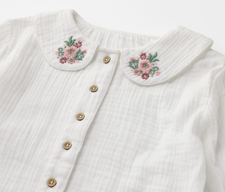 Detail einer Kinder-Musselin-Bluse mit Blumenstickerei am Kragen und Knöpfen.