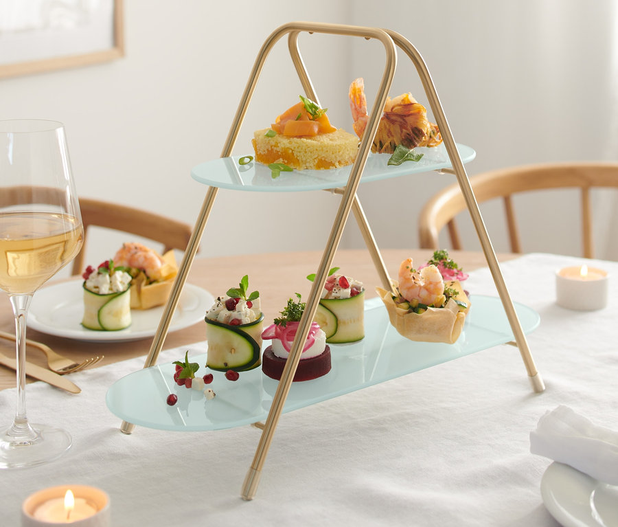 Zweistöckige Etagere mit verschiedenen Häppchen auf einem festlich gedeckten Tisch.