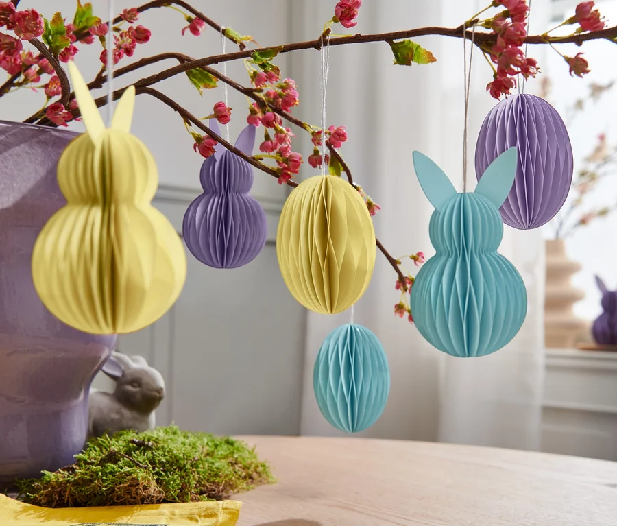 Gelbe, lila und blaue 6 Papier-Osteranhänger hängen an einem blühenden Zweig.