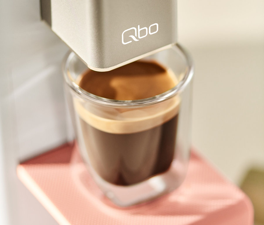 Qbo ICONIC x Pantone Special Edition Muted Clay Kaffeemaschine füllt eine Tasse Kaffee.