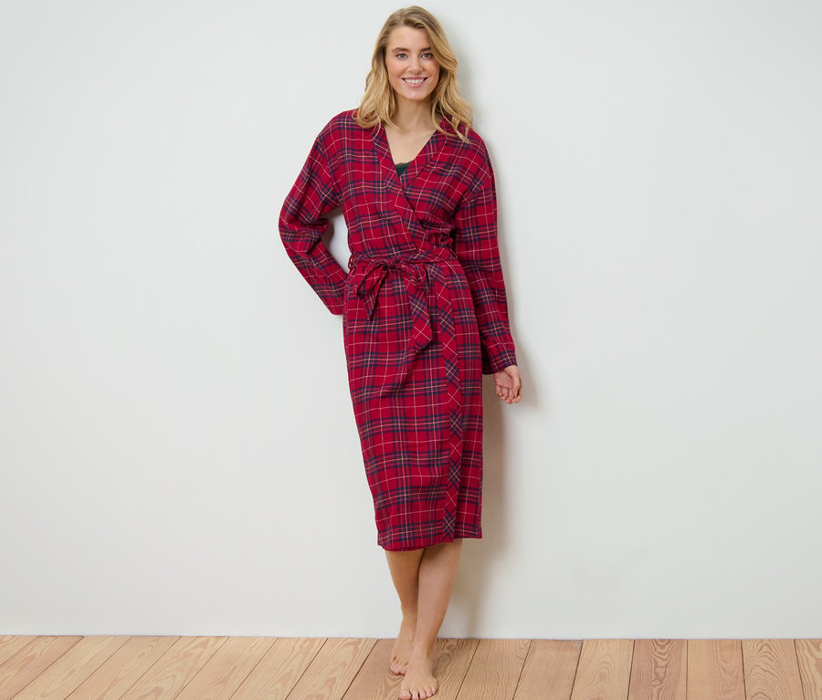 Blonde Frau steht und trägt einen rot karierten Flanell-Morgenmantel.