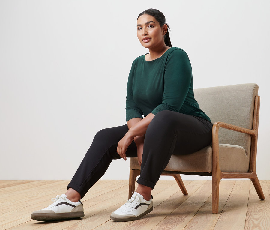 Frau sitzt im Sessel und trägt ein dunkelgrünes Shirt mit 3/4-Arm.