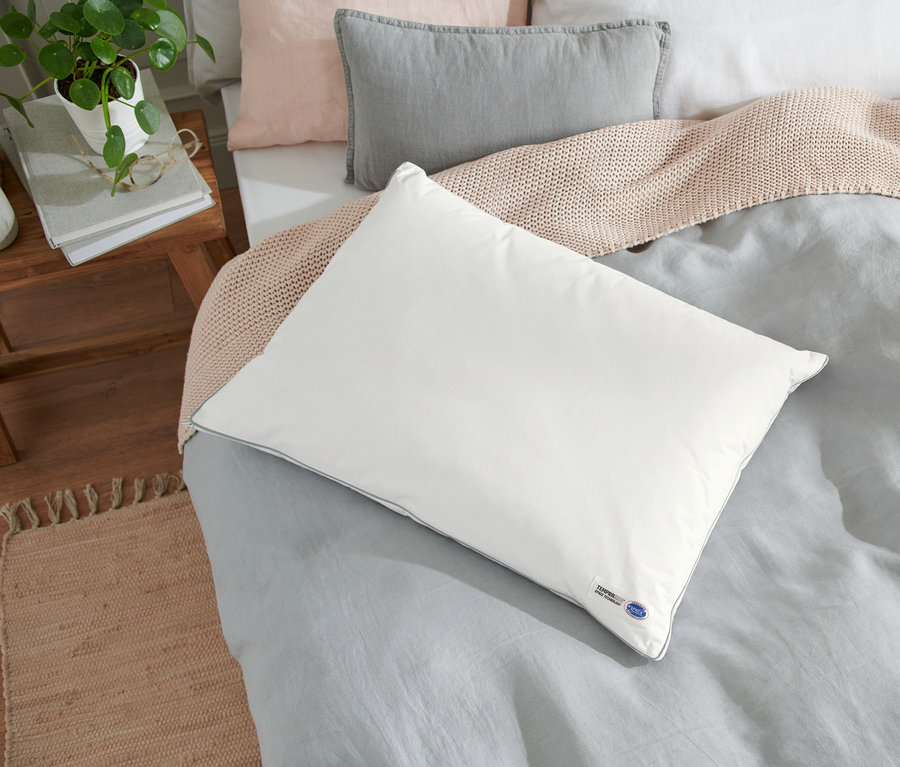 Weißes Temprakon Ergonomic Kissen liegt auf einem Bett mit grauer Bettwäsche.